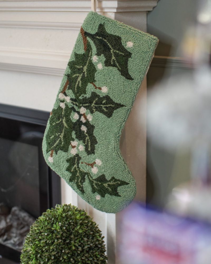 Green Christmas stocking with holly design hanging on a fireplace – LNH Edit