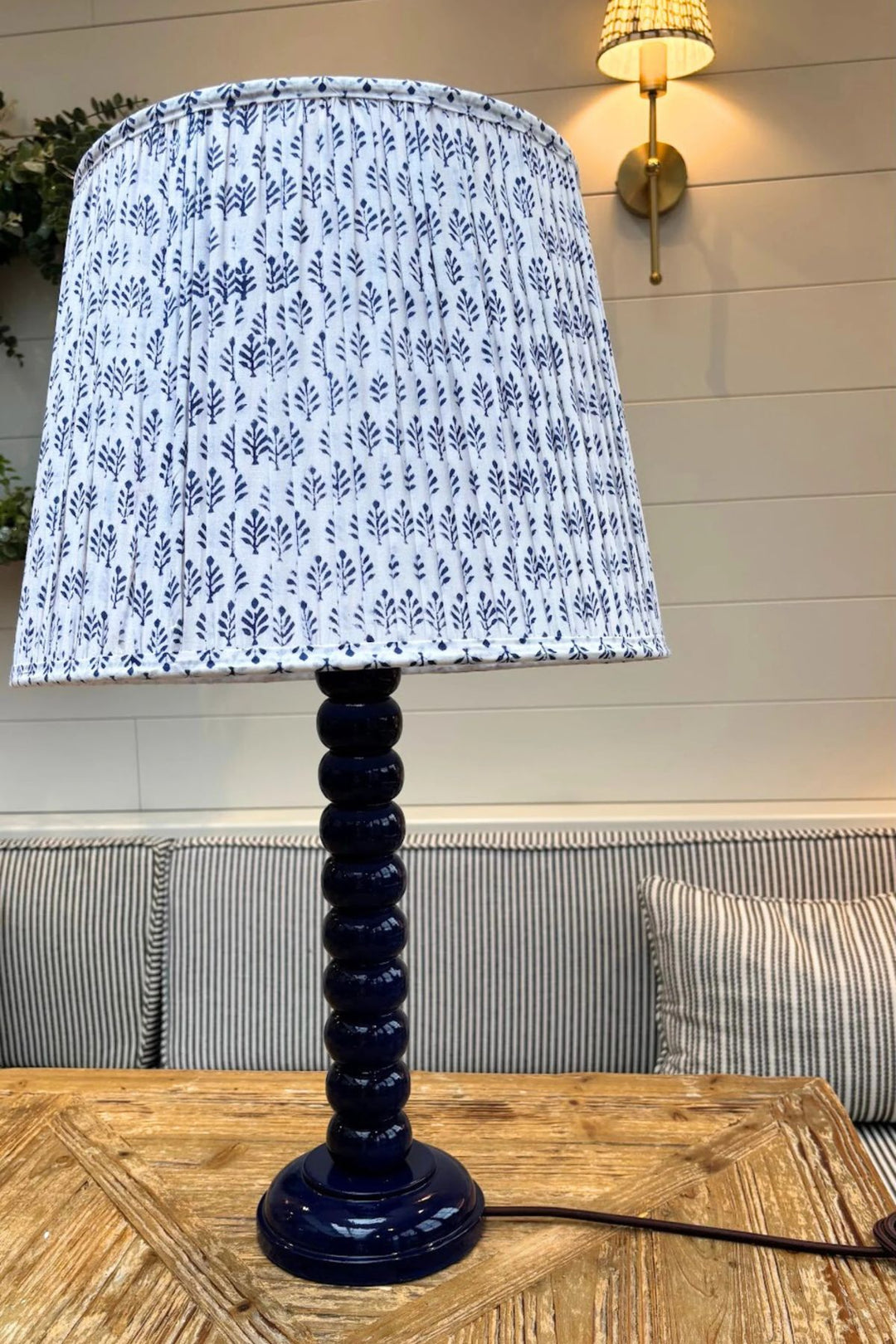 Hand-painted tall bobbin lamp base in blue gloss with pleated Sofia Blue lampshade, styled on wooden table.