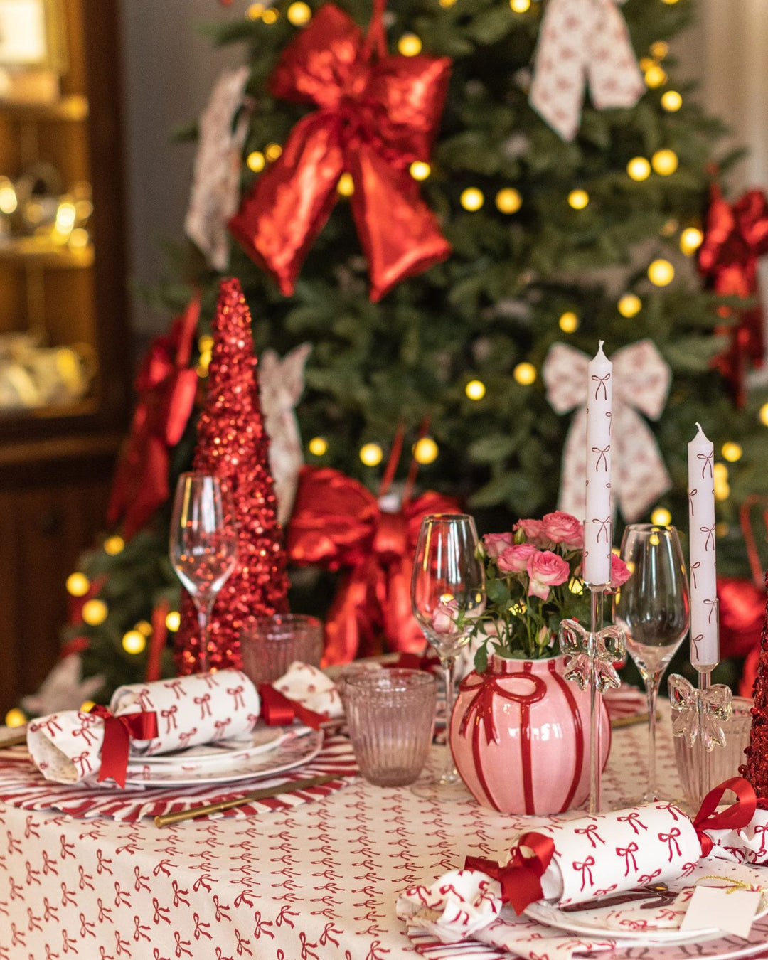 Christmas bow napkins styled with festive red and pink table setting, candles, and tree decor.