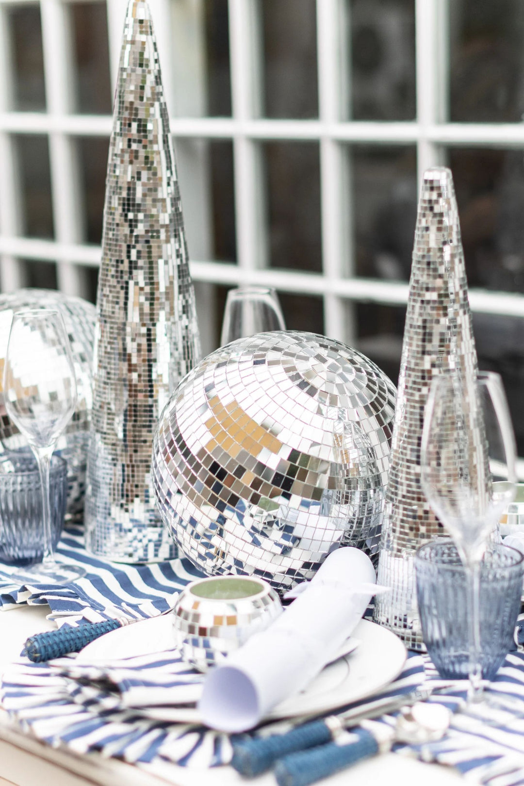 Modern festive tablescape with LNH Edit blue striped napkins, glassware, and silver disco decorations creating a chic holiday dining look.