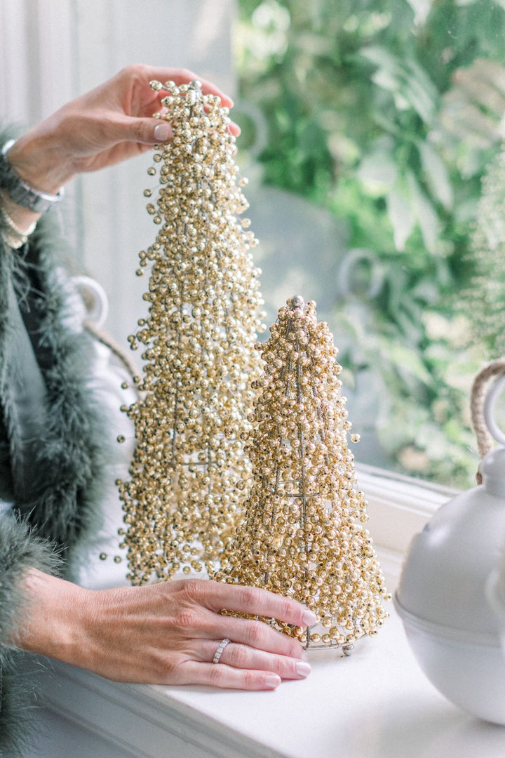 Gold beaded Christmas tree decoration styled on a windowsill, held by a person in a cosy festive home setting.