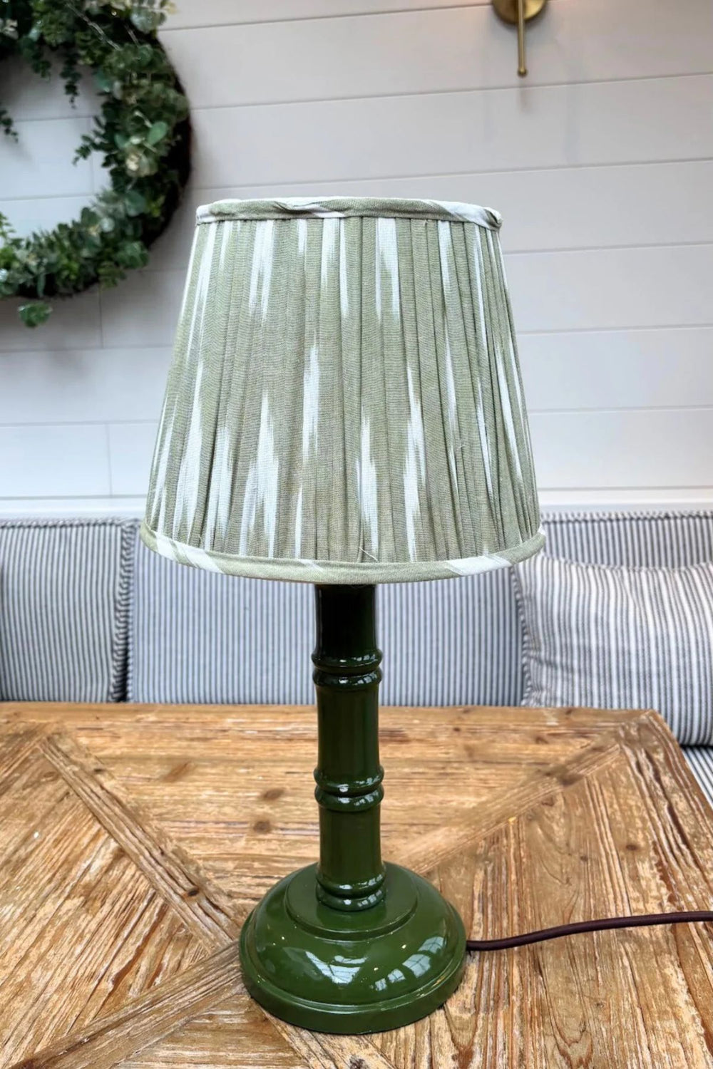 Green hand-painted bamboo lamp base with pleated lampshade on wooden table in a cosy interior