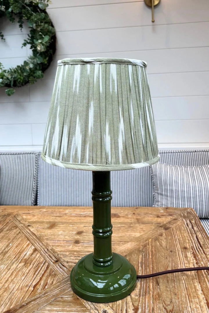 Green hand-painted bamboo lamp base with pleated lampshade on wooden table in a cosy interior