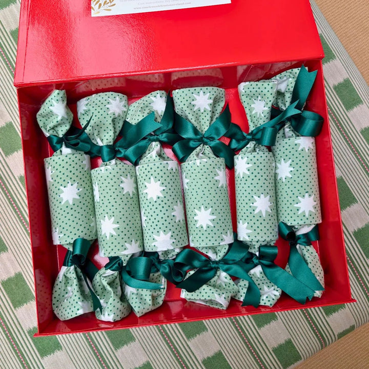 Green and white star-print Christmas crackers tied with green ribbons, presented in a red gift box by LNH Edit.