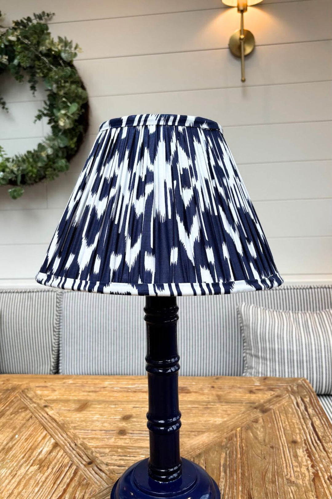 Hand-painted blue bamboo lamp base with pleated navy ikat lampshade on wooden table.