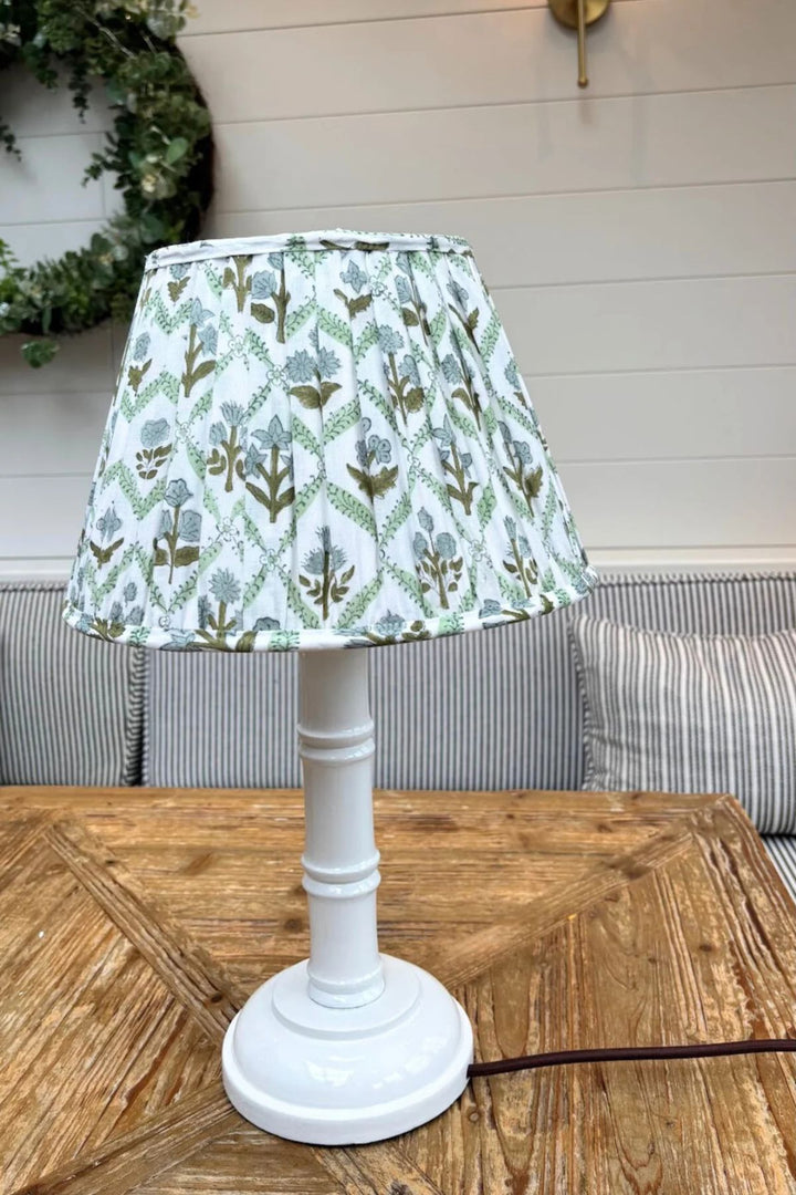 Hand painted white gloss bamboo lamp base with pleated green floral lampshade styled on a wooden table.