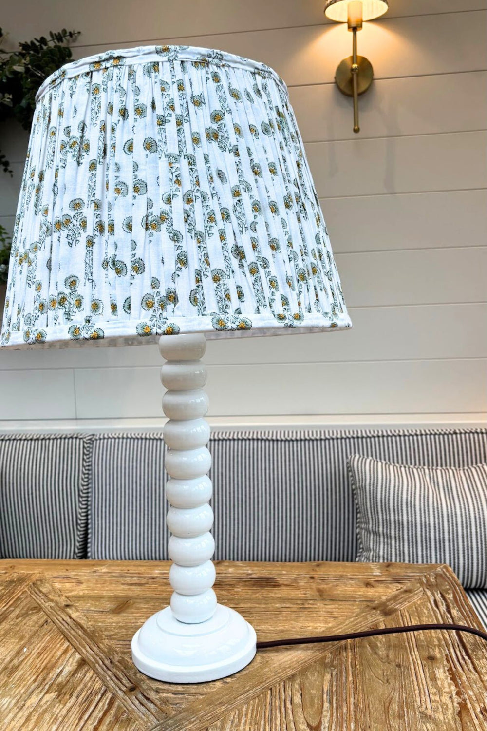 White gloss hand-painted bobbin tall lamp base with Lennox pleated lampshade on wooden table.