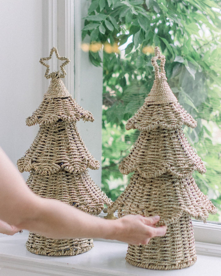 Two handwoven rattan Christmas trees with stars styled on a windowsill with greenery.