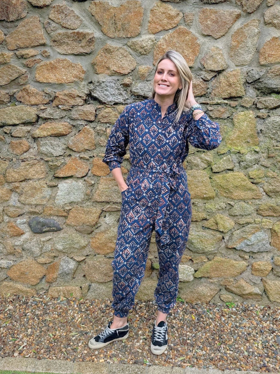 Woman wearing the Hazel Navy handcrafted long sleeve jumpsuit standing against a stone wall.