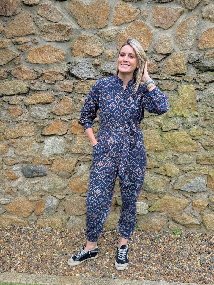 Woman wearing the Hazel Navy handcrafted long sleeve jumpsuit standing against a stone wall.