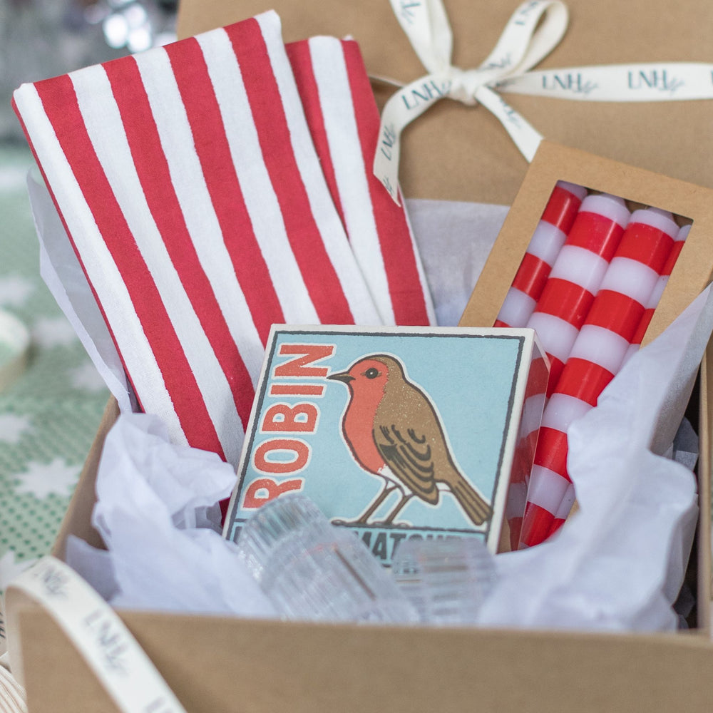 Close-up of LNH Edit Holiday Hostess Gift Box with striped candles, robin matchbox, and hand-printed napkins.