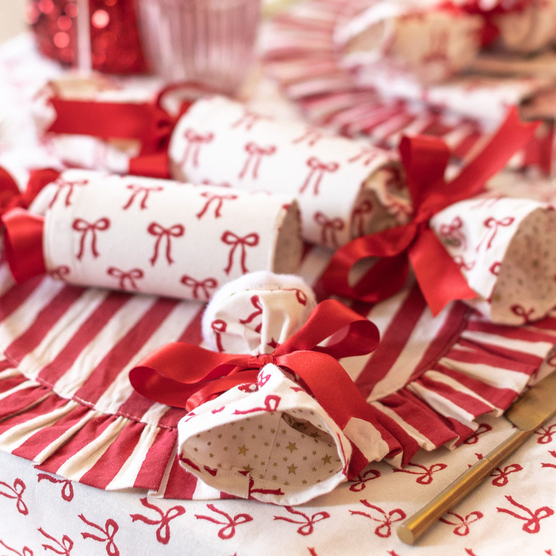 Red and white bow print Christmas crackers on striped placemats from The Holly Collection by LNH Edit.