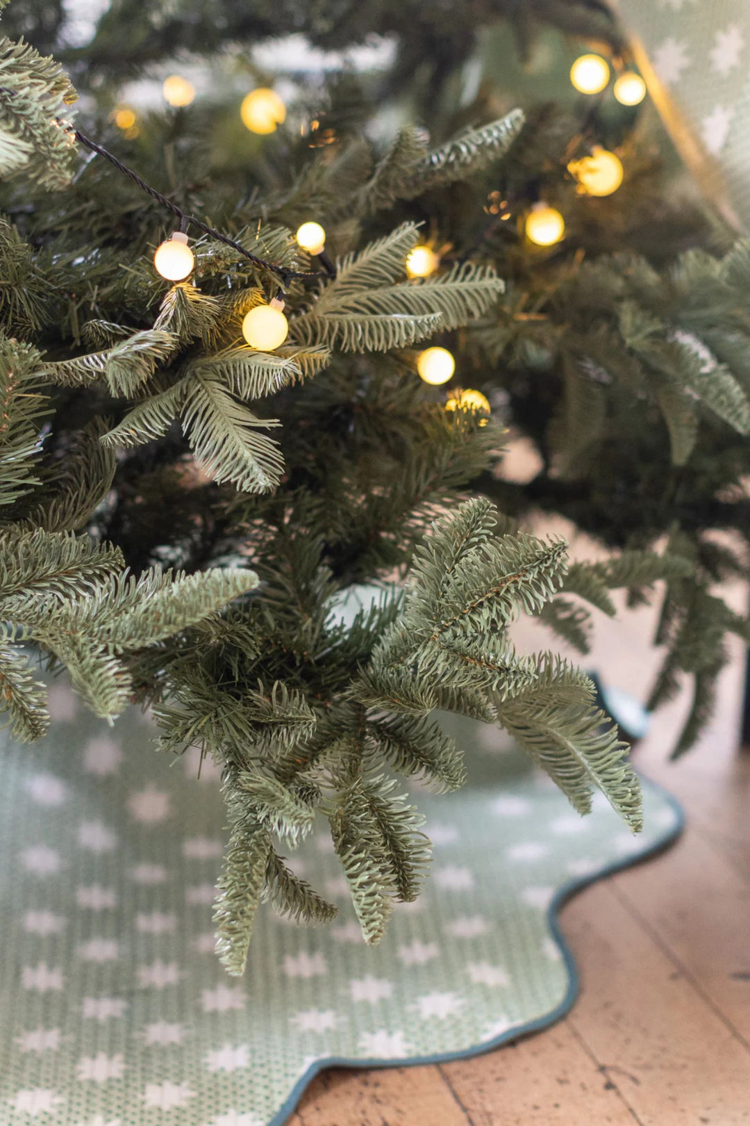 LNH Edit Mistletoe green star hand block-printed quilted Christmas tree skirt styled under festive tree with warm lights.