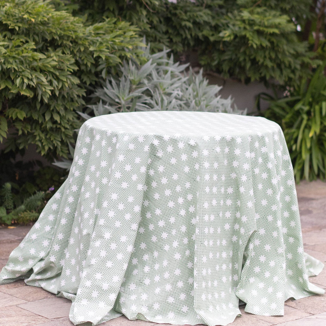 LNH Edit Mistletoe green star block-printed round cotton tablecloth styled outdoors with draped fabric and greenery background.