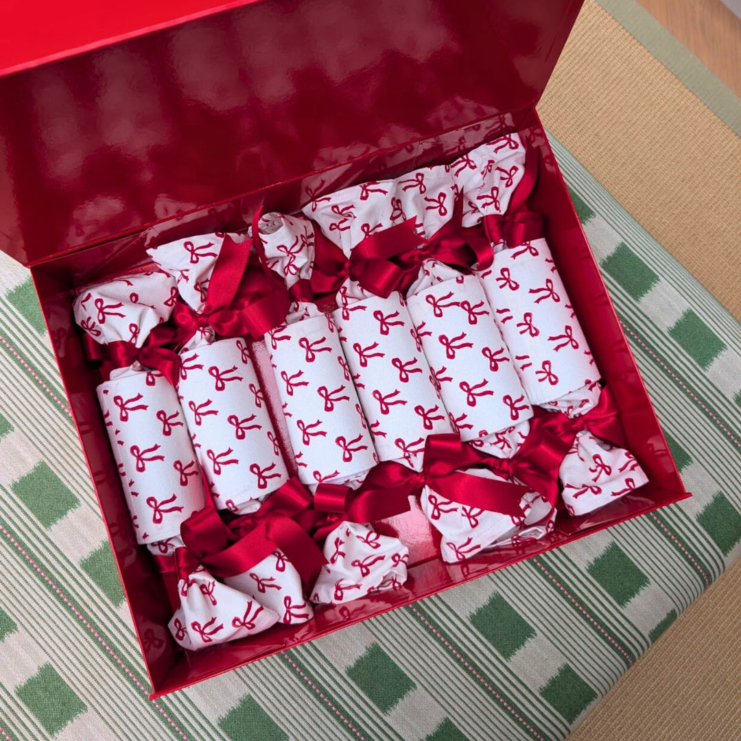 Red and white bow-print Christmas crackers tied with red ribbons, arranged in a glossy red gift box by LNH Edit.