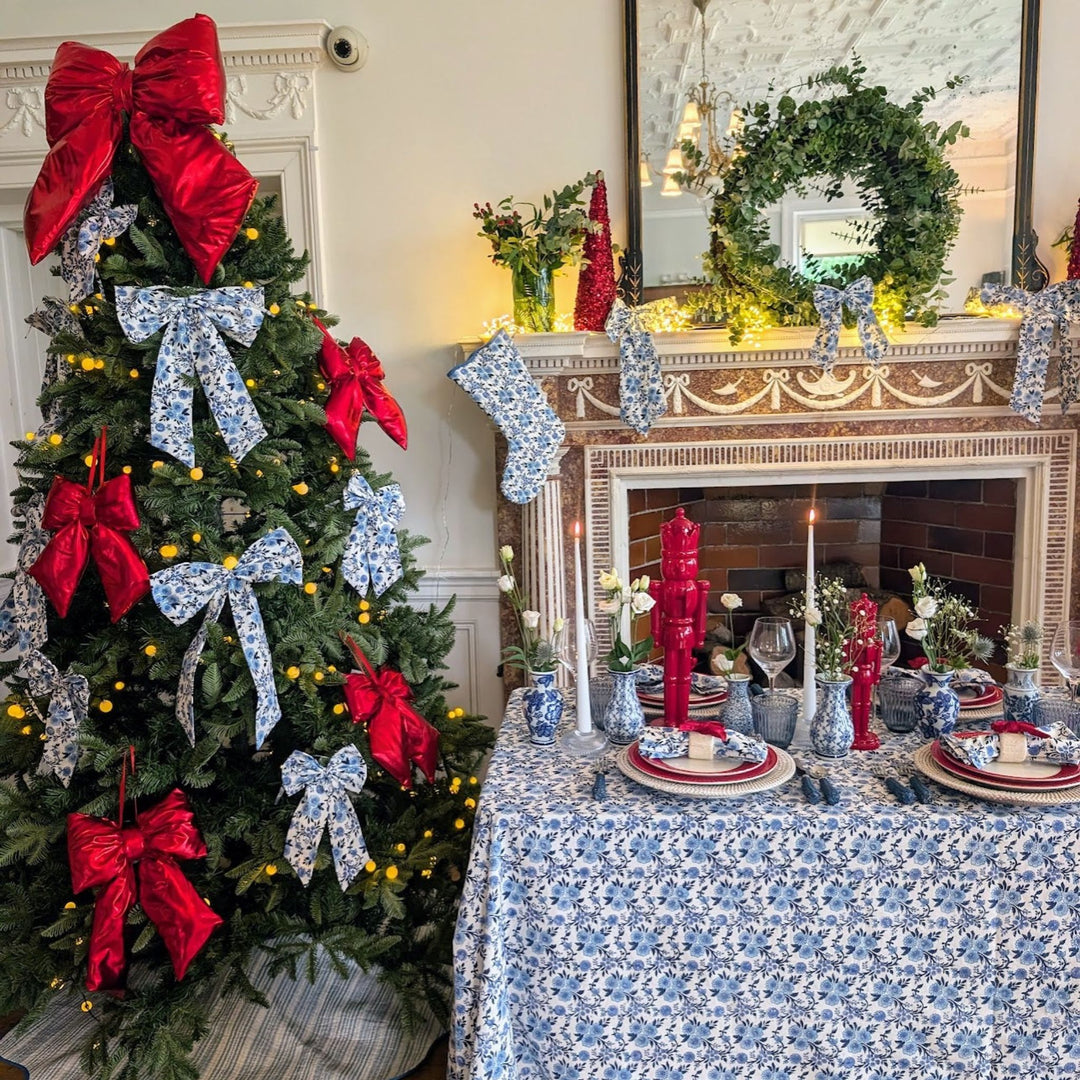 LNH Edit Thistle Christmas tablescape featuring a blue floral tablecloth, red bows, and festive fireplace styling with candles and greenery.