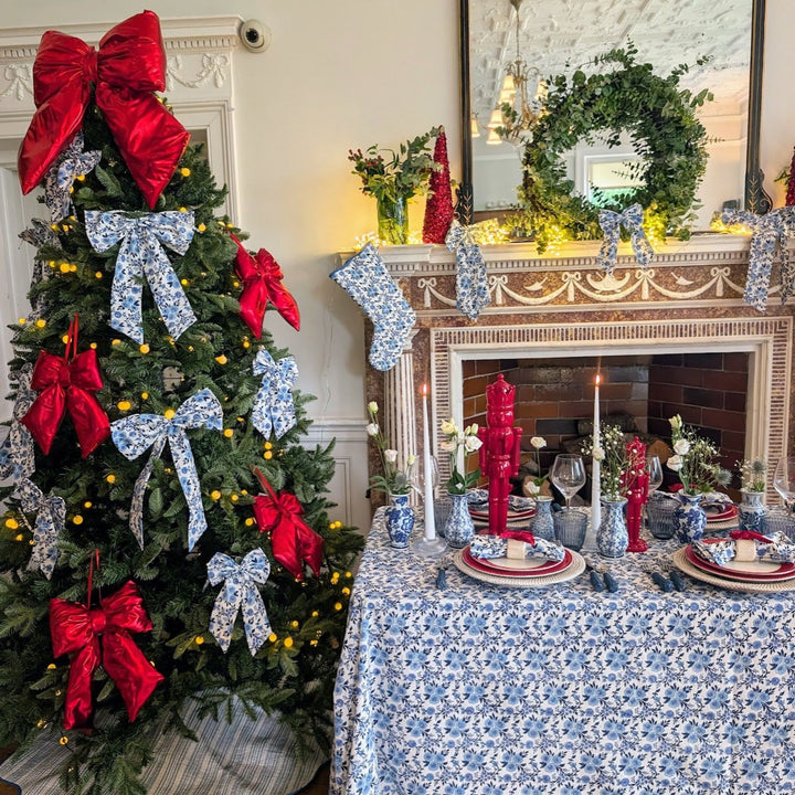 LNH Edit Thistle Christmas tablescape featuring a blue floral tablecloth, red bows, and festive fireplace styling with candles and greenery.