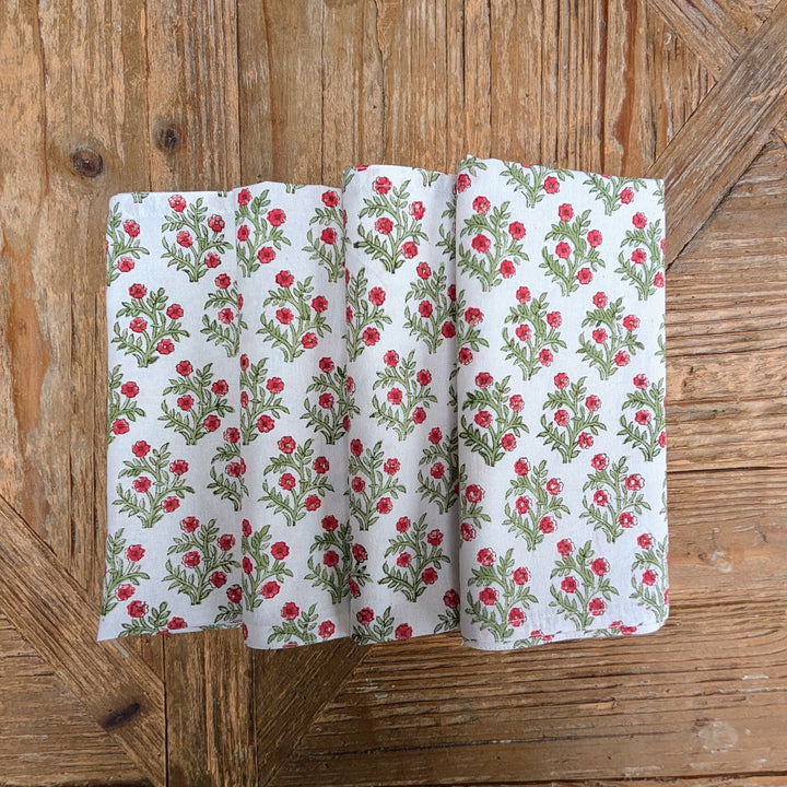 Set of four hand block printed green and red floral Christmas napkins on wooden table.