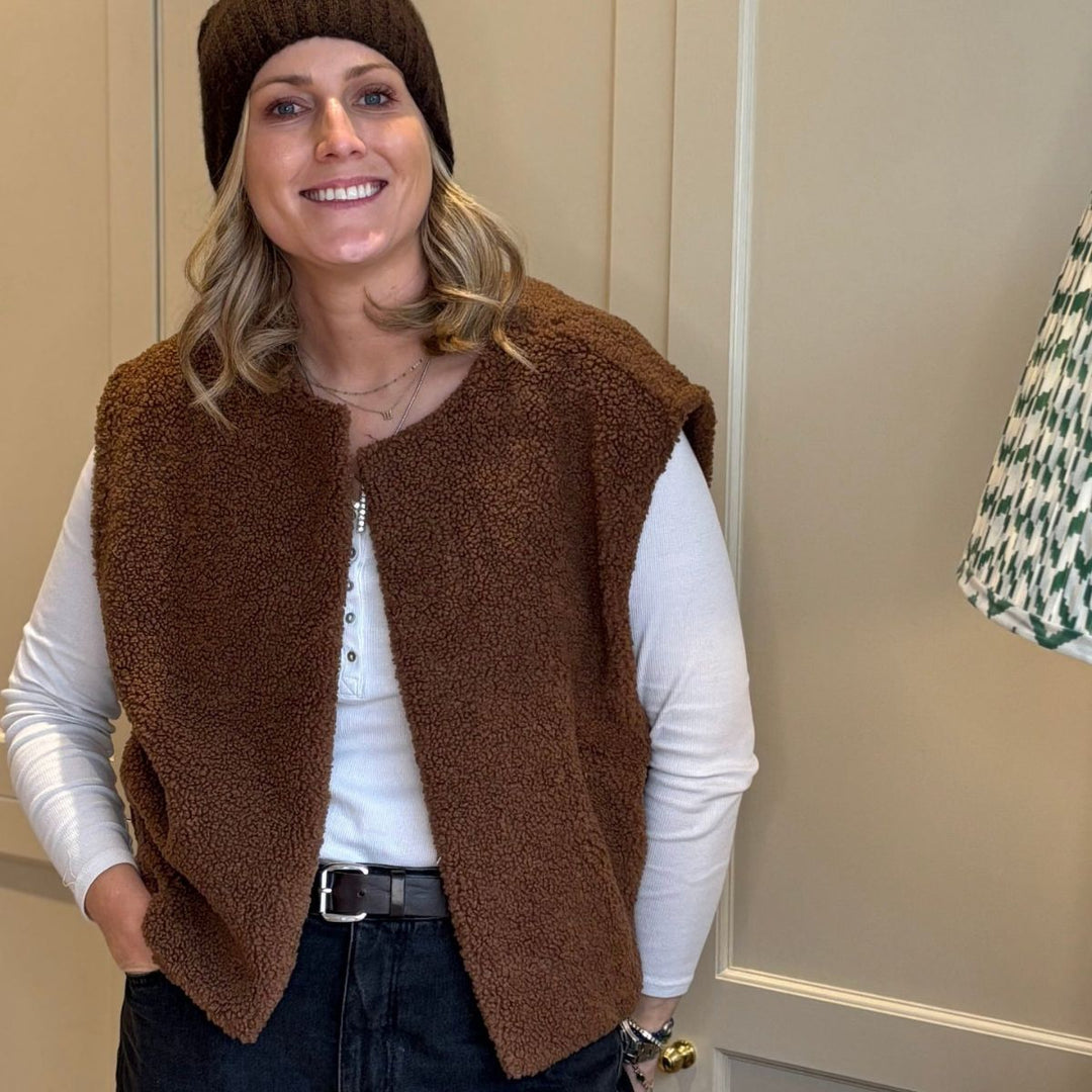 Laura, founder of LNH Edit, in a brown sherpa vest and beanie — casual studio portrait for LNH Edit.