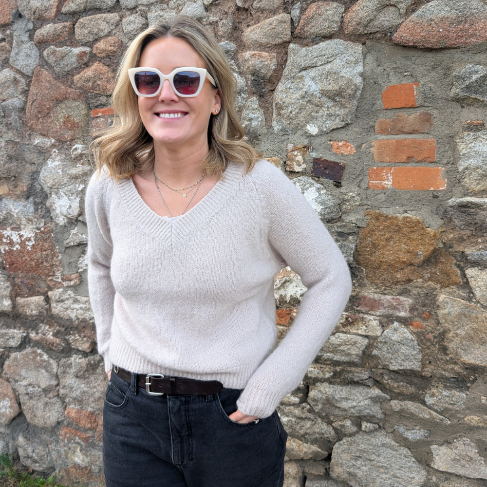 Laura, founder of LNH Edit, standing against a stone wall wearing a cream knit and sunglasses.