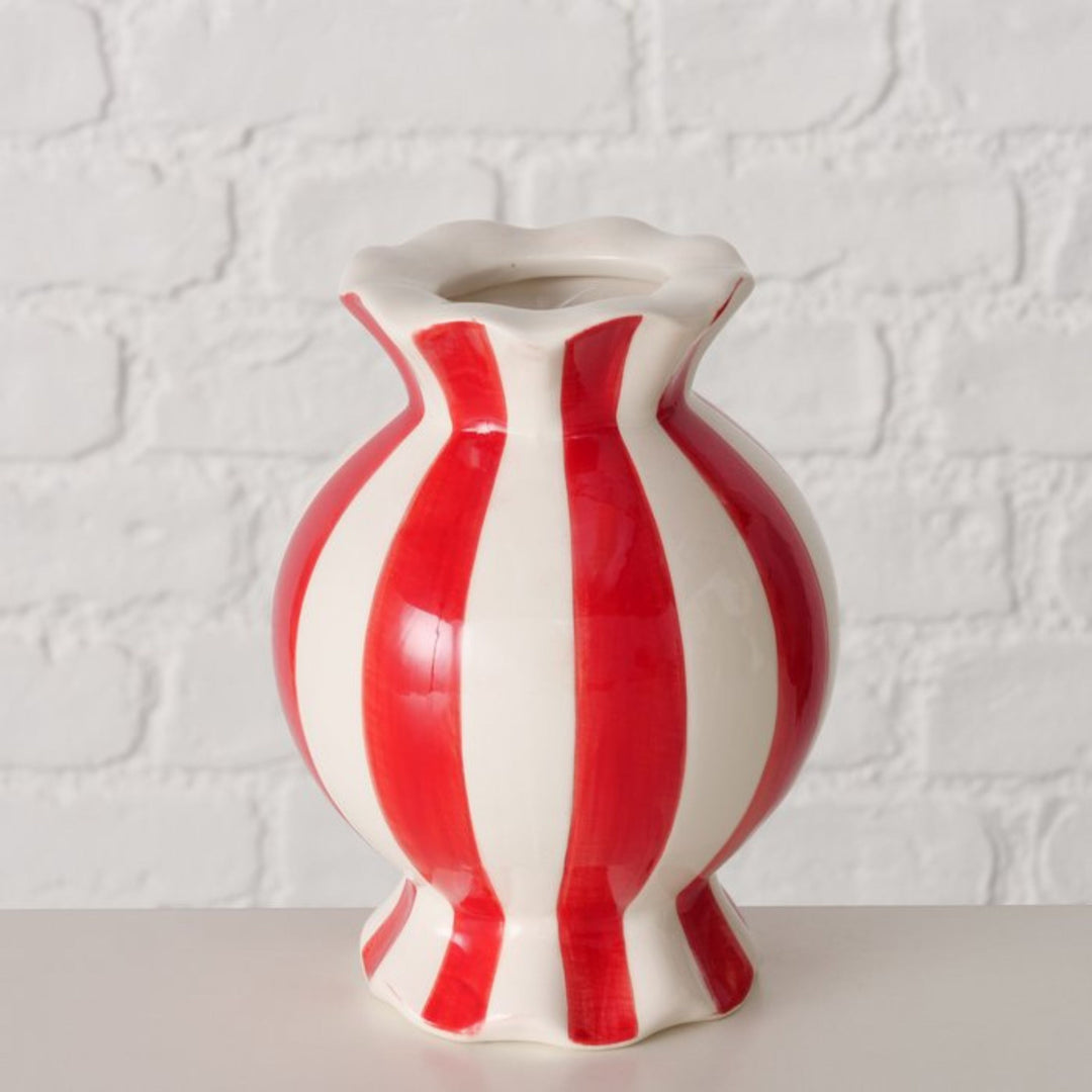Candy stripe ceramic vase in red and white displayed against white brick wall.”