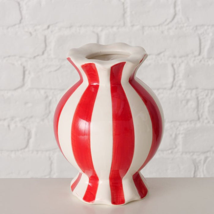 Candy stripe ceramic vase in red and white displayed against white brick wall.”