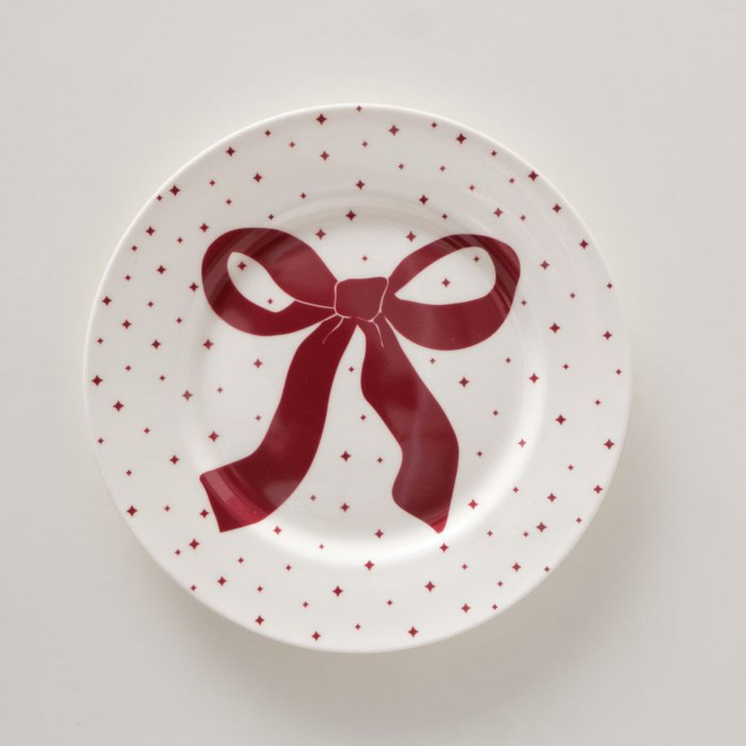 Overhead flat lay of white ceramic plate with red bow design.