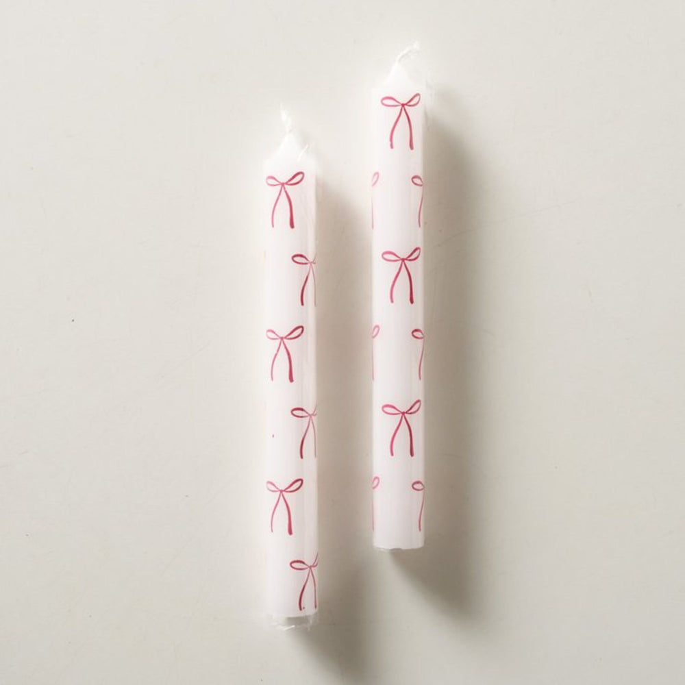 Two white taper candle featuring red bow pattern detail.