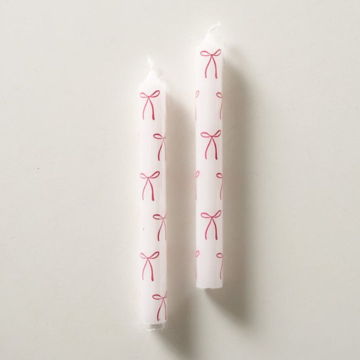 Two white taper candle featuring red bow pattern detail.