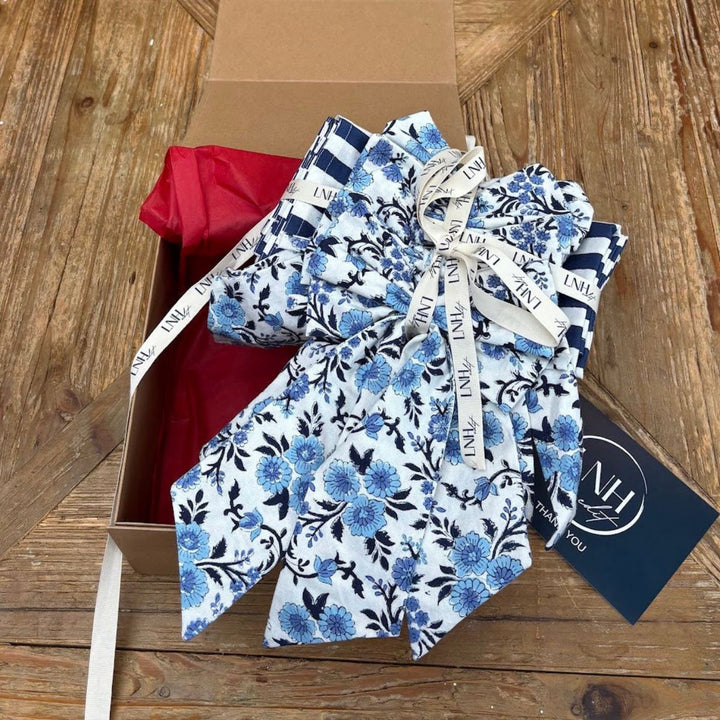 LNH Edit Thistle Hosting Gift Box with blue floral napkins, striped napkins and four thistle bows styled in brown gift box with red tissue paper.