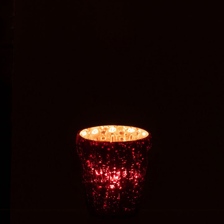 Red glass tealight holder glowing softly in a dark setting, creating a festive warm light.