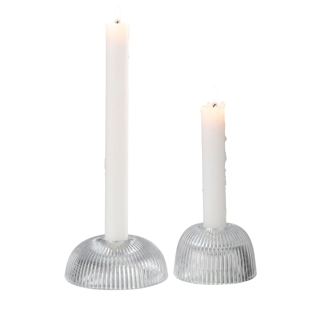 Two ribbed clear glass candle holders with lit white taper candles.