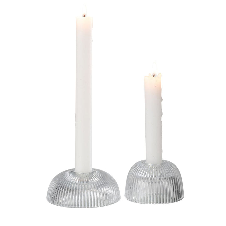 Two ribbed clear glass candle holders with lit white taper candles.
