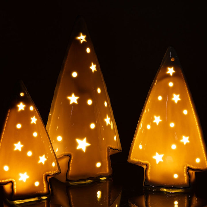 Trio of ceramic LED trees glowing warmly in the dark with star cut-outs.