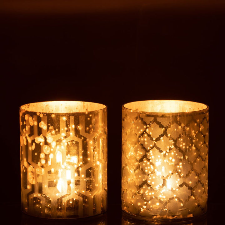 Two silver patterned candle holders illuminated in a dark setting, creating a warm festive glow.