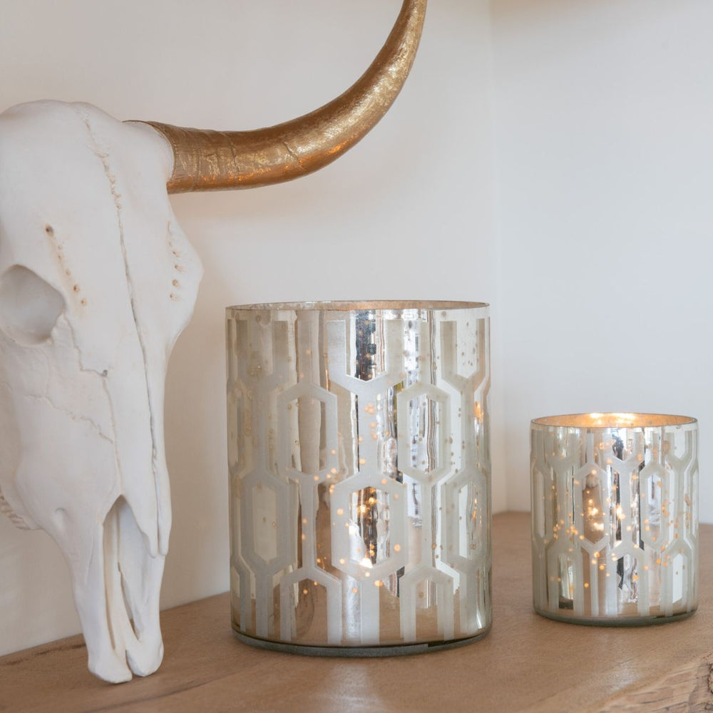 Silver patterned glass candle holders styled on a wooden shelf beside a decorative skull sculpture.