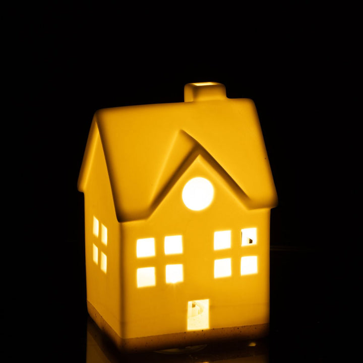 White ceramic LED house glowing warmly in the dark, soft Christmas lighting.