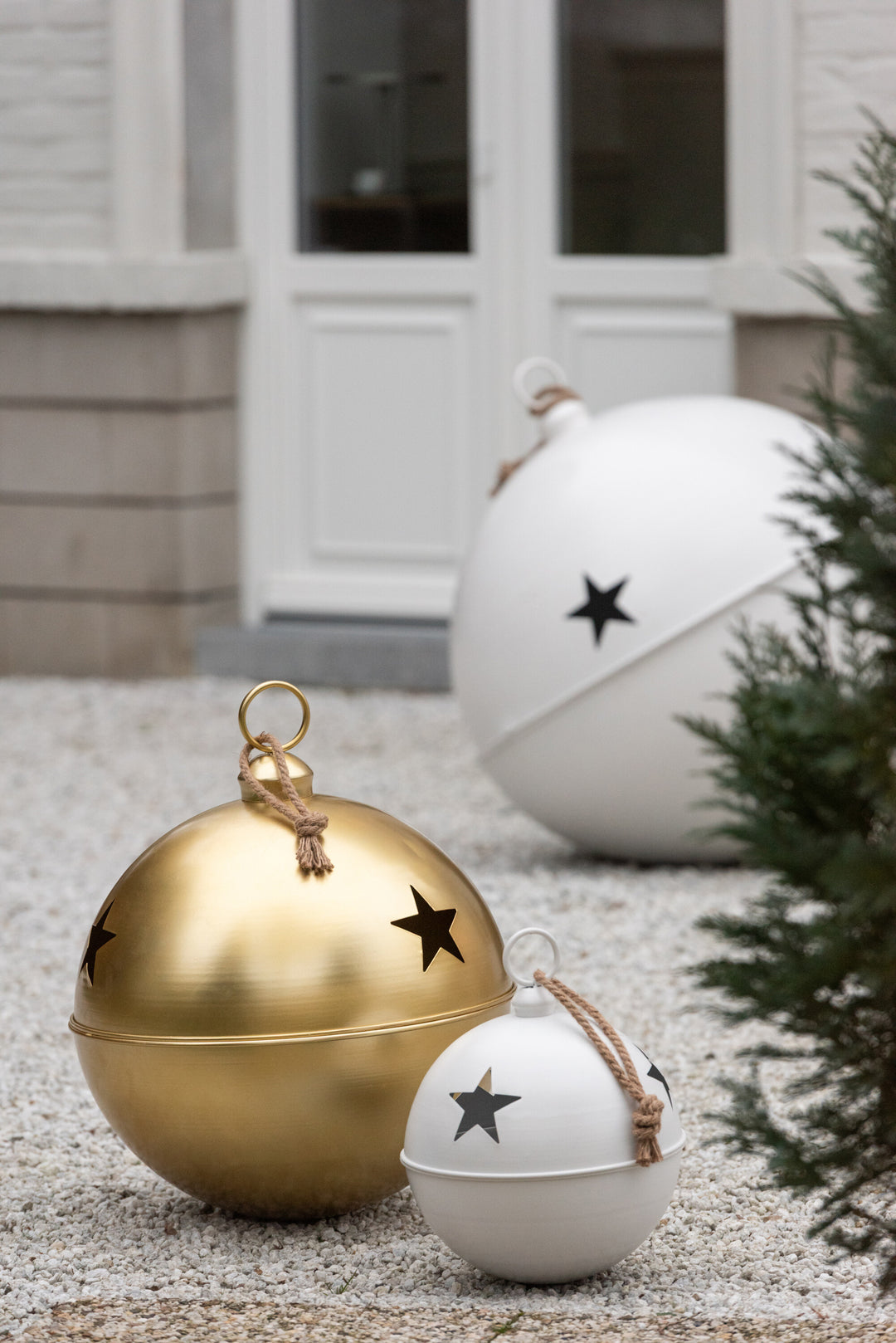 White and gold iron star baubles styled outdoors with festive greenery, modern Christmas styling.